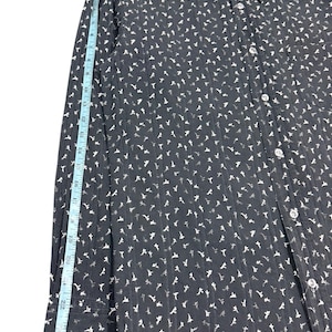 May include: A black long-sleeve button-down shirt with a white floral pattern and vertical textured stripes. A light blue measuring tape is placed along the sleeve, showing a length of approximately 26 inches from the shoulder seam to the cuff.