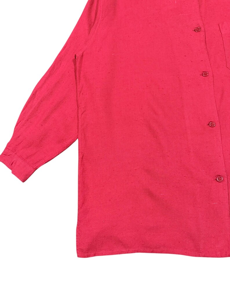 Puede incluir: Una camisa roja brillante de manga larga con botones en la parte delantera y un bolsillo en el pecho. La camisa tiene un aspecto texturizado y un cuello cl&aacute;sico. La manga est&aacute; abotonada en el pu&ntilde;o.