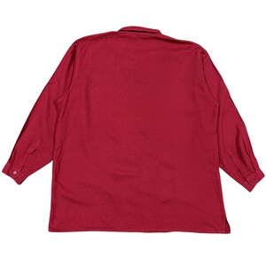 Puede incluir: Una camisa de manga larga con botones en un tono rojo intenso liso. La camisa presenta un cuello cl&aacute;sico y pu&ntilde;os abotonados. La tela parece ser un material ligero, adecuado para climas c&aacute;lidos.