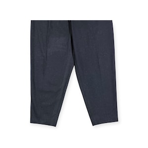 Puede incluir: Un pantal&oacute;n de color gris carb&oacute;n oscuro que presenta un sutil patr&oacute;n moteado en toda la tela. El pantal&oacute;n tiene un corte de pierna recta con un pliegue vertical visible que recorre el centro de cada pierna, ofreciendo un aspecto estructurado.