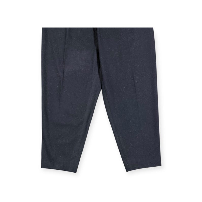 Puede incluir: Un pantal&oacute;n de color gris carb&oacute;n oscuro que presenta un sutil patr&oacute;n moteado en toda la tela. El pantal&oacute;n tiene un corte de pierna recta con un pliegue vertical visible que recorre el centro de cada pierna, ofreciendo un aspecto estructurado.