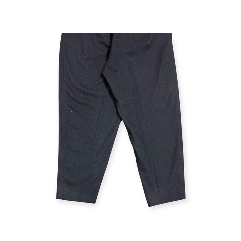 Puede incluir: Un pantal&oacute;n de color gris carb&oacute;n oscuro que presenta una textura sutilmente moteada en toda la tela. El pantal&oacute;n tiene un corte recto con una raya central visible que recorre la parte delantera de cada pierna, dando un aspecto estructurado.