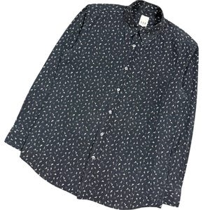 May include: A long-sleeved button-down shirt in black with a repeating white pattern of small Eiffel Tower icons. The shirt features a standard collar, a front button placket with white buttons, and a single chest pocket on the left side.