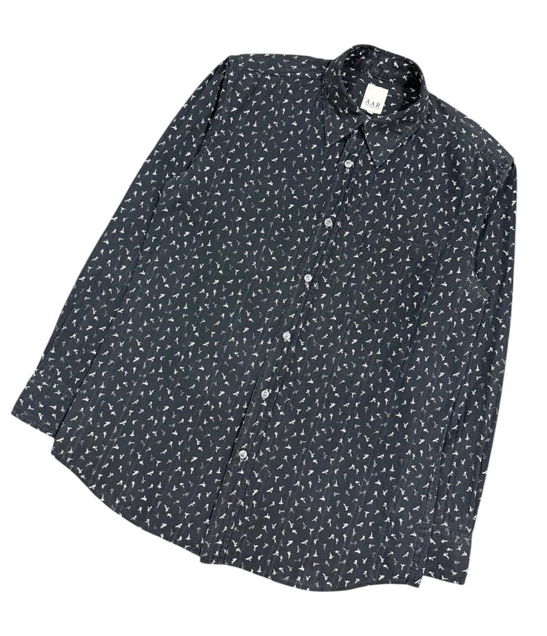 May include: A long-sleeved button-down shirt in black with a repeating white pattern of small Eiffel Tower icons. The shirt features a standard collar, a front button placket with white buttons, and a single chest pocket on the left side.
