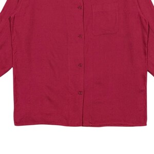 Puede incluir: Camisa de manga larga en un tono rojo intenso. Presenta una botonadura frontal, un bolsillo en el pecho y un cuello cl&aacute;sico. La tela parece ser un material suave y tejido. Las mangas terminan en pu&ntilde;os abotonados.