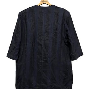 May include: A dark navy blue blazer with a collarless, open-front design and three-quarter length sleeves. The garment features a subtle, vertical striped texture throughout the fabric and is displayed on a wooden hanger labeled French Connection.