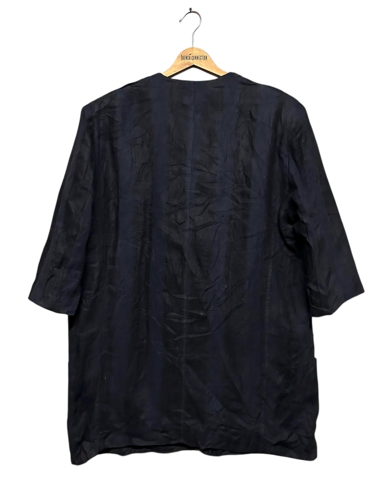 May include: A dark navy blue blazer with a collarless, open-front design and three-quarter length sleeves. The garment features a subtle, vertical striped texture throughout the fabric and is displayed on a wooden hanger labeled French Connection.