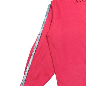 Puede incluir: Una camisa roja de manga larga con cuello, con una cinta m&eacute;trica que muestra la longitud de la manga. La manga mide aproximadamente 58 cm.