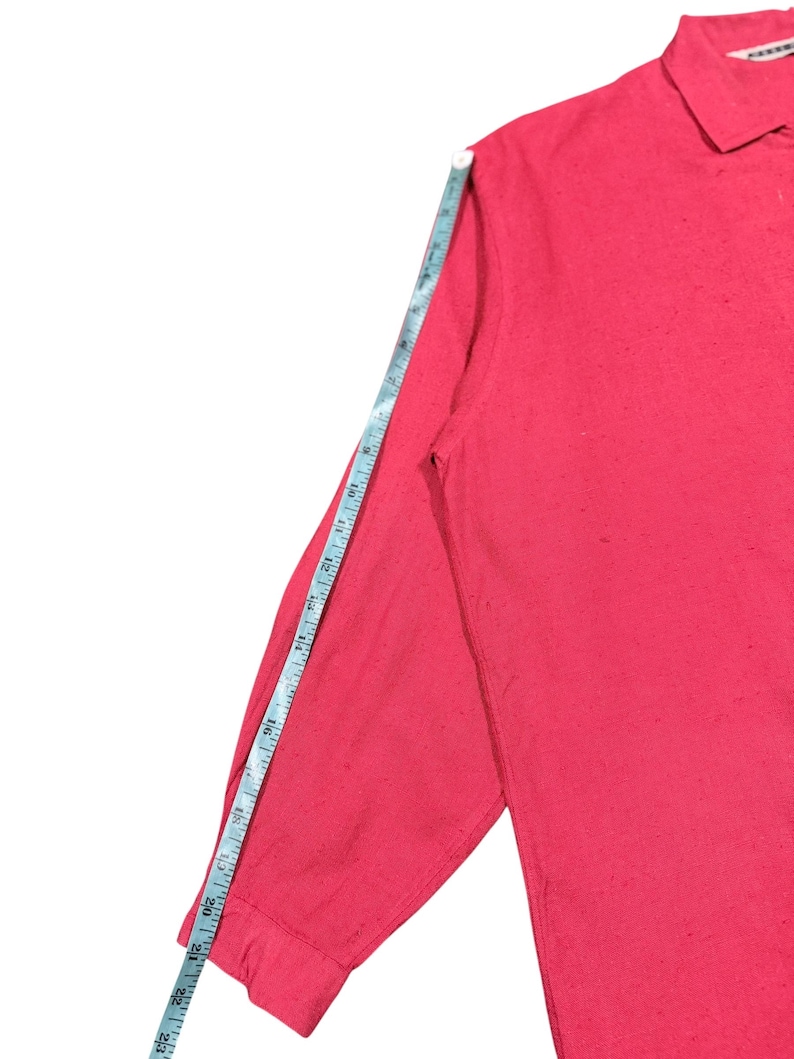 Puede incluir: Una camisa roja de manga larga con cuello, con una cinta m&eacute;trica que muestra la longitud de la manga. La manga mide aproximadamente 58 cm.