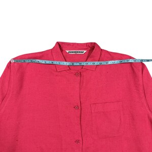 Puede incluir: Una camisa rosa brillante con botones y un bolsillo en el pecho. La camisa mide aproximadamente 48 cm de ancho en el pecho. El cuello tiene una etiqueta blanca con texto negro.