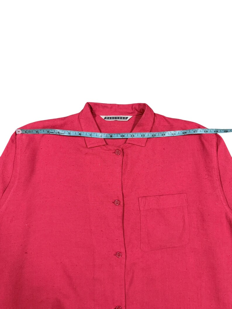 Puede incluir: Una camisa rosa brillante con botones y un bolsillo en el pecho. La camisa mide aproximadamente 48 cm de ancho en el pecho. El cuello tiene una etiqueta blanca con texto negro.