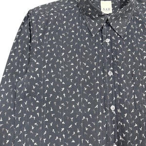 May include: A dark gray long-sleeve button-down shirt featuring a repeating white floral pattern and vertical textured stripes. The shirt has a standard collar, a front button placket with clear buttons, and a chest pocket. A label reads A.A.R.