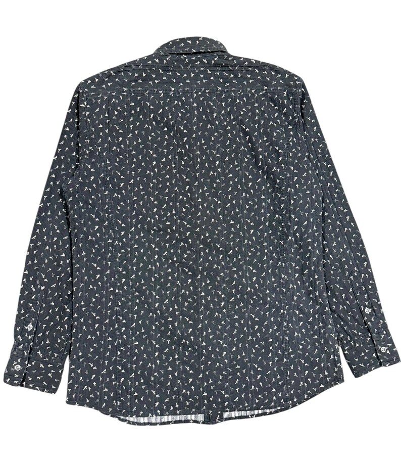 May include: A long-sleeve button-down shirt in a dark charcoal gray color featuring a repeating white pattern of small, stylized bird silhouettes. The garment includes a standard collar, a buttoned front placket, and cuffs with two buttons each.
