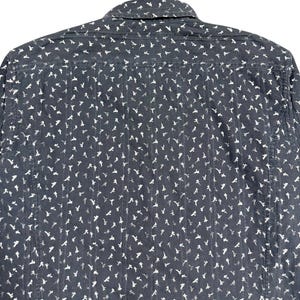 May include: A dark charcoal gray long-sleeve shirt featuring a repeating white floral pattern and vertical textured stripes. The garment includes a standard collar, a back yoke, and a button-down construction with a consistent all-over print.