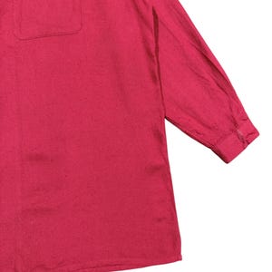 Puede incluir: Una camisa roja de manga larga con un bolsillo en el pecho. La camisa tiene un pu&ntilde;o abotonado y una tela ligeramente texturizada. La prenda es de color liso y parece estar hecha de un material ligero.