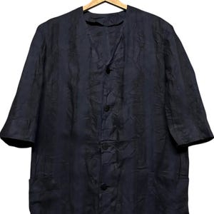 May include: A dark navy blue button-down shirt with a textured, crinkled fabric finish. The shirt features a V-neckline, elbow-length sleeves, and two lower front pockets. It is displayed on a wooden hanger labeled French Connection.