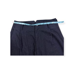 Puede incluir: Pantalones azul marino oscuro con cierre de bot&oacute;n, trabillas para cintur&oacute;n y pliegues frontales. Una cinta m&eacute;trica azul claro se coloca sobre la cintura, indicando una medida de aproximadamente 40,6 cm en la parte superior.