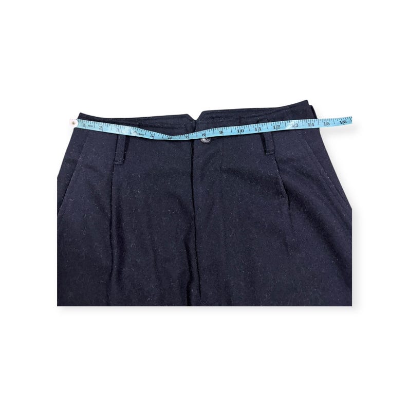 Puede incluir: Pantalones azul marino oscuro con cierre de bot&oacute;n, trabillas para cintur&oacute;n y pliegues frontales. Una cinta m&eacute;trica azul claro se coloca sobre la cintura, indicando una medida de aproximadamente 40,6 cm en la parte superior.