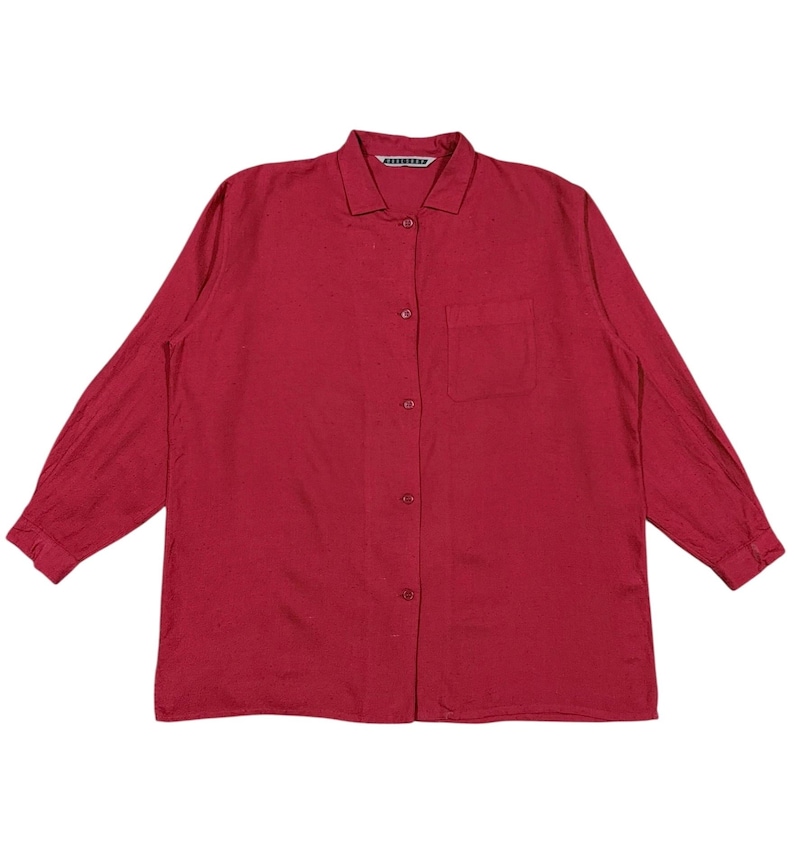 Puede incluir: Una camisa abotonada de manga larga en un tono rojo intenso. La camisa presenta un cuello cl&aacute;sico, un bolsillo en el pecho y botones en la parte delantera. La tela parece ser ligera.