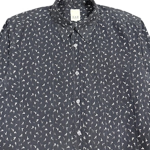 May include: A dark charcoal gray long-sleeve button-down shirt featuring a repeating white floral pattern and vertical textured stripes. The shirt includes a standard collar, a front chest pocket, and a white label with the text A.A.R.