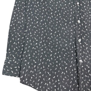 May include: A long-sleeved button-down shirt in a dark charcoal gray color featuring a repeating pattern of small white floral shapes and vertical textured stripes. The garment includes a standard collar, a front button placket, and cuffs.
