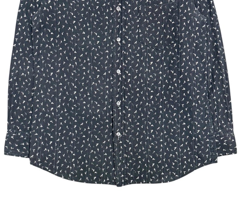 May include: A dark charcoal gray long-sleeve button-down shirt featuring a repeating white bird pattern and vertical pinstripes. The shirt includes a front chest pocket on the left side, a standard collar, and white buttons running down the center.