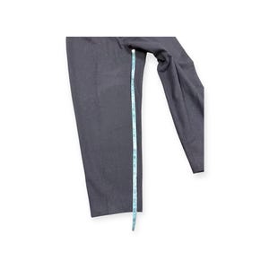 Puede incluir: Un pantal&oacute;n de color gris carb&oacute;n oscuro con corte de pierna recta. Una cinta m&eacute;trica de color azul claro est&aacute; colocada verticalmente a lo largo de la pierna, indicando una medida de longitud de aproximadamente 61 cent&iacute;metros en total.