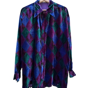 Pode incluir: Uma camisa de manga comprida com textura de veludo e um padrão de losangos repetitivo em tons de roxo profundo, verde esmeralda e azul real. A peça inclui um colarinho pontiagudo, punhos abotoados e uma carcela de botões frontal.
