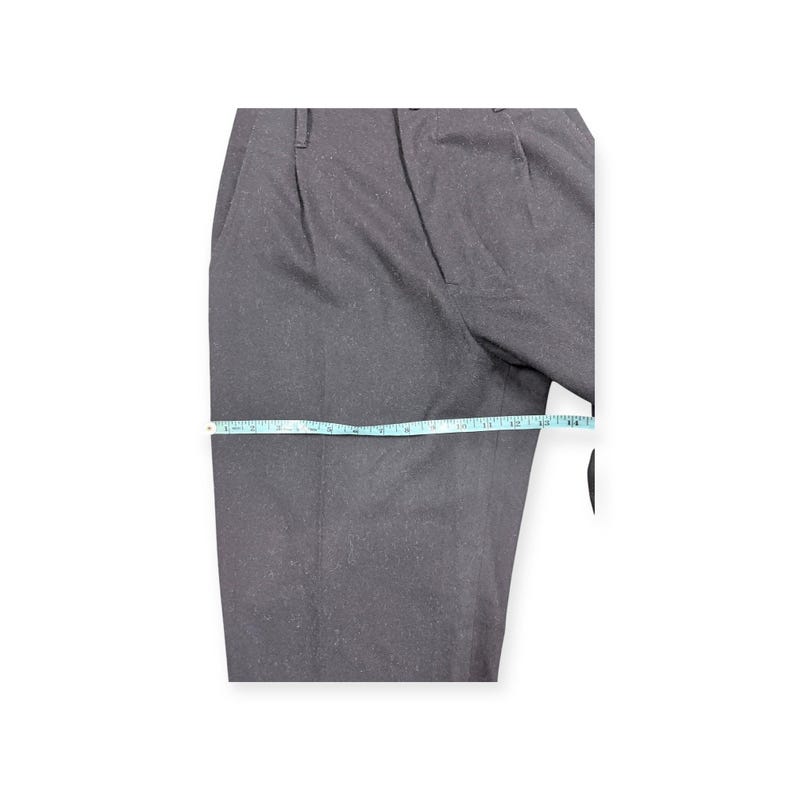 Puede incluir: Pantalones de color gris oscuro con una textura ligeramente moteada y un dise&ntilde;o frontal plisado. Una cinta m&eacute;trica de color azul claro se coloca horizontalmente sobre el muslo, indicando un ancho de unos 35,5 cm en la tela.