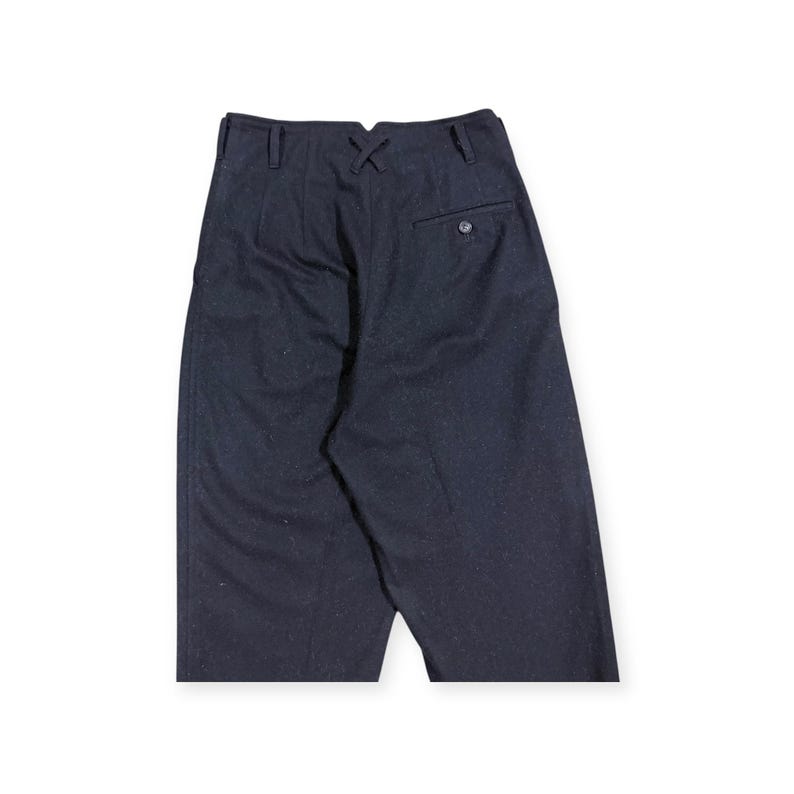 Puede incluir: Pantalones de talle alto en azul marino oscuro con una distintiva muesca en forma de V en el centro de la cintura trasera, trabillas para cintur&oacute;n y un bolsillo ribeteado en el lado derecho con cierre de bot&oacute;n. La tela tiene textura moteada.