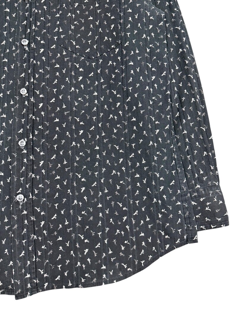 May include: A dark gray long-sleeve button-down shirt featuring a repeating white floral pattern and vertical pinstripes. The garment includes a front chest pocket, a standard collar, and light-colored buttons running down the front placket.