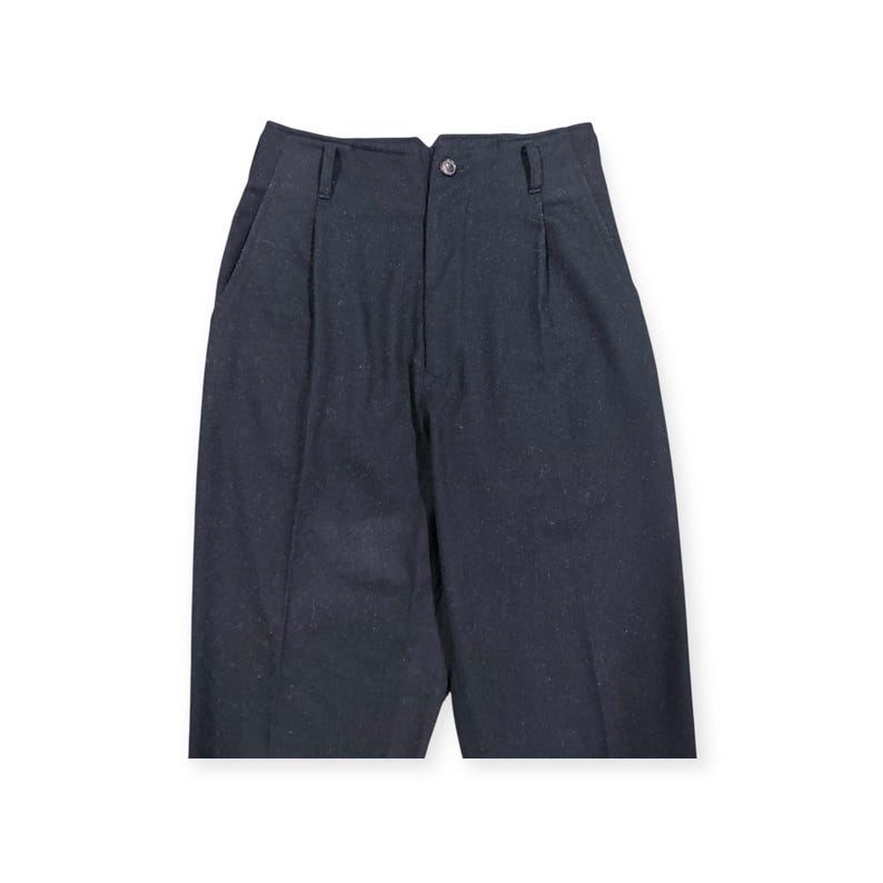 Puede incluir: Pantalones de talle alto en tela gris carb&oacute;n oscuro con una textura sutilmente moteada. Estos pantalones cuentan con cierre de bot&oacute;n frontal, cremallera, trabillas para cintur&oacute;n en la cintura y pliegues verticales que bajan desde la cintura.