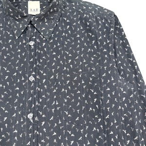 May include: A dark charcoal gray long-sleeve button-down shirt featuring a repeating white floral pattern and vertical pinstripes. The shirt includes a standard collar, a front chest pocket, and a label at the neck with the text A.A.R.