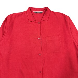 Puede incluir: Una camisa roja brillante con botones, cuello y un bolsillo en el pecho. La camisa tiene mangas largas y una tela texturizada. El nombre de la marca es visible en el cuello.