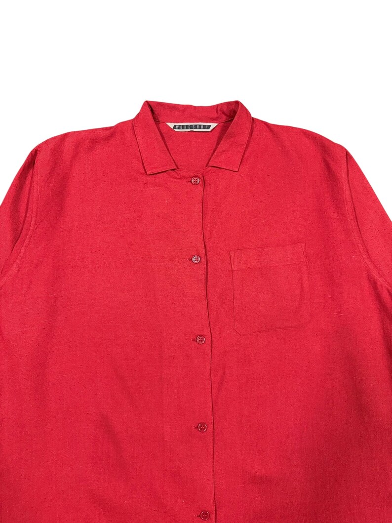 Puede incluir: Una camisa roja brillante con botones, cuello y un bolsillo en el pecho. La camisa tiene mangas largas y una tela texturizada. El nombre de la marca es visible en el cuello.