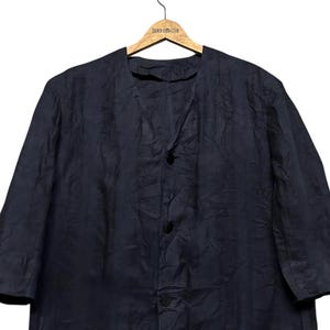 May include: A dark navy blue jacket with a collarless V-neckline and three black buttons down the front. The garment features a textured, slightly wrinkled fabric finish and three-quarter length sleeves, hanging on a wooden clothes hanger.
