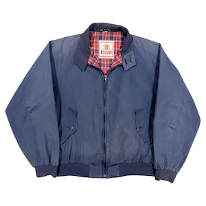 Könnte beinhalten: Eine marineblaue Jacke mit Reißverschluss und einem rot-grün-blau karierten Innenfutter. Die Jacke hat einen spitzen Kragen, zwei Vordertaschen mit Knopfverschluss sowie gerippte Bündchen und Saum. Ein weißes Etikett zeigt den Schriftzug B IGGIO.