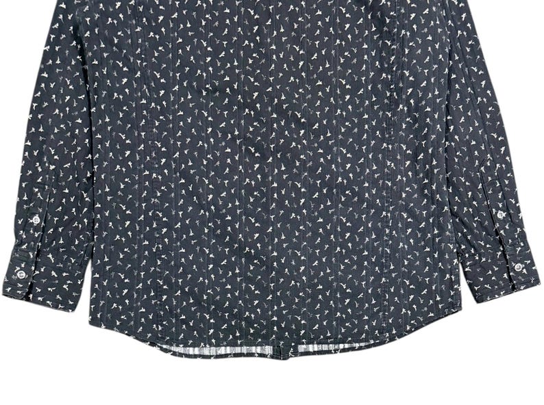 May include: A long-sleeve button-down shirt in dark charcoal gray featuring a repeating pattern of small white bird silhouettes and thin vertical pinstripes. The garment includes a standard collar, a front button placket, and cuffs with buttons.