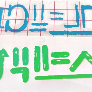 May include: Two vinyl decal stickers on a white backing sheet. The top decal is bright blue and features stylized text with a grid overlay. The bottom decal is bright green and features stylized text with a horizontal line underneath the characters.