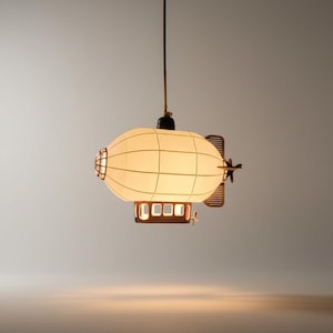 May include: A distinctive zeppelin-shaped pendant light. The cream-coloured, oval shade features a grid pattern, and is set within a brown metal frame. The fixture includes a propeller and a small, rectangular base, suspended from a single cable.