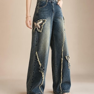 Può includere: Jeans blu a gamba larga con ricamo a farfalla sul davanti. I jeans presentano dettagli strappati lungo le cuciture e toppe. Vita alta e cintura decorativa. Lavaggio vintage.