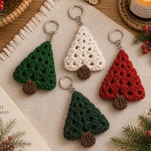 May include: Four crochet Christmas tree keychains in green, white, and red yarn. Each triangular tree features a brown crocheted trunk and a silver metal keyring attached to the top. The designs are crafted with an openwork stitch pattern.
