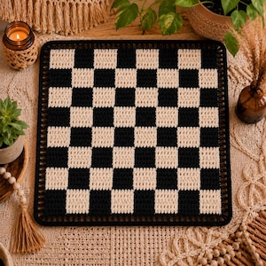 May include: A square crochet mat featuring a black and cream checkerboard pattern. The mat has a solid black border with evenly spaced vertical stitches along the entire perimeter, creating a structured edge for this textile piece.
