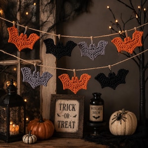 May include: A decorative garland featuring six crocheted bat ornaments in orange, black, and grey, suspended from a thin twine string. The bats are arranged in two rows, showcasing detailed yarn textures and distinct wing shapes for each individual piece.