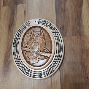 May include: A wooden cribbage board with an owl carved into the center. The board is oval shaped and has a dark brown stain.