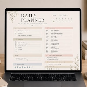 以下が含まれることがあります： ラップトップの画面には、「Daily Planner」が表示され、優先事項、To-Doリスト、スケジュールが表示されています。画面には2024年5月20日の日付が表示されています。プランナーは、キャンドル、ノート、コーヒーマグの隣にあります。