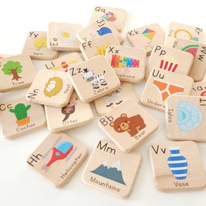 May include: Wooden alphabet blocks with illustrations and letter pairings. The blocks feature images of a submarine, tree, cactus, egg, zebra, otter, bear, helicopter, mountains, vase, apple, and more.