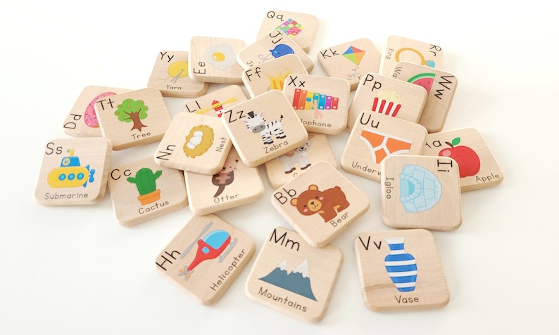 May include: Wooden alphabet blocks with illustrations and letter pairings. The blocks feature images of a submarine, tree, cactus, egg, zebra, otter, bear, helicopter, mountains, vase, apple, and more.