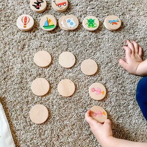 May include: Wooden matching game with colorful illustrations of a hot air balloon, sailboat, airplane, and other objects. The game includes blank wooden circles and a child's hand holding a matching piece.