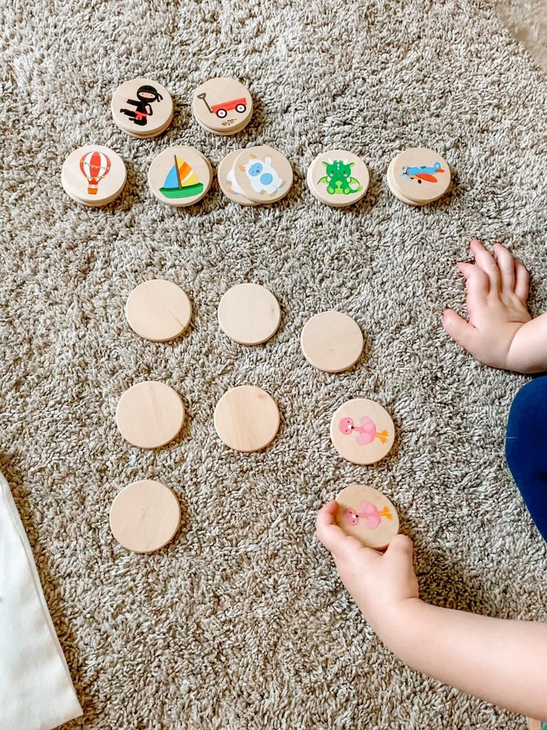 May include: Wooden matching game with colorful illustrations of a hot air balloon, sailboat, airplane, and other objects. The game includes blank wooden circles and a child's hand holding a matching piece.